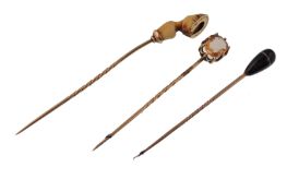 Three 19th century gold cravat stick pins. The pins having decorative finials to include a banded