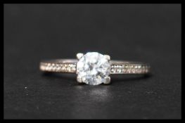 A hallmarked 9ct white gold and CZ ring having a central round cut  CZ with CZ set shoulders.