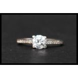 A hallmarked 9ct white gold and CZ ring having a central round cut  CZ with CZ set shoulders.