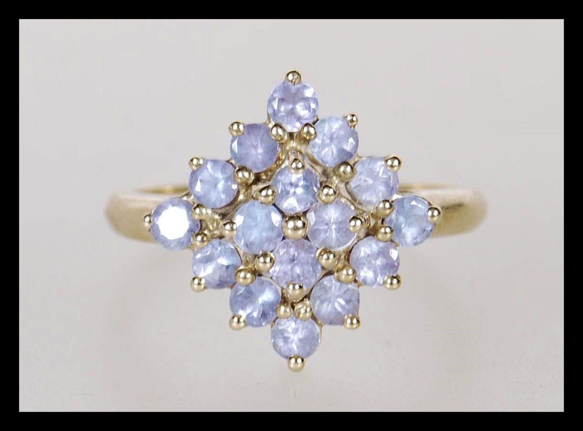 A hallmarked 9ct gold ladies cluster ring prong set with lilac stones in a geometric formation.
