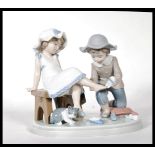 A Lladro ceramic figure group titled ' Try this One ', (5361) of a young girl trying on a shoe.