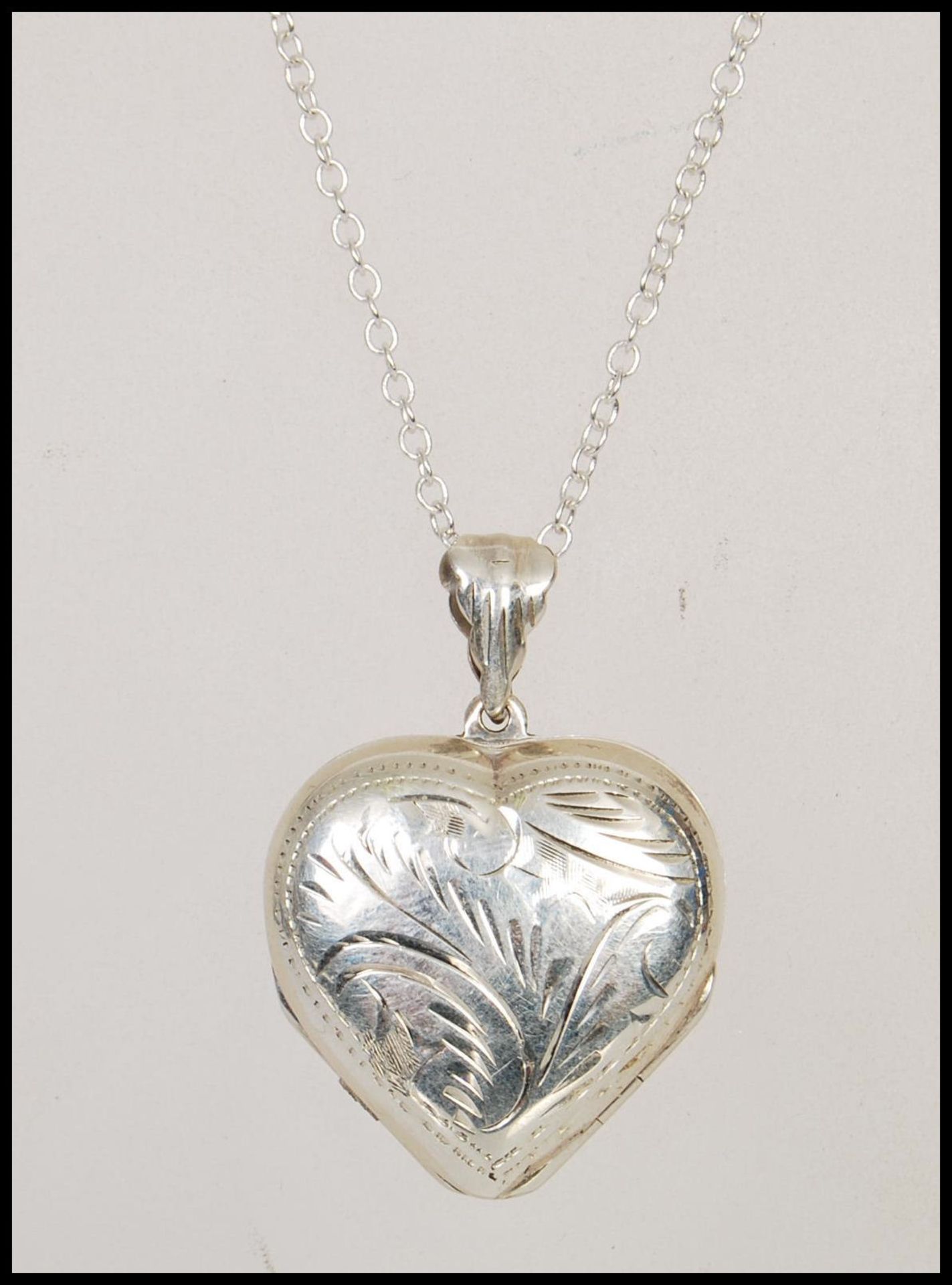 A double sided silver heart shaped locket having engraved decoration to both sides. Stamped 925 on a