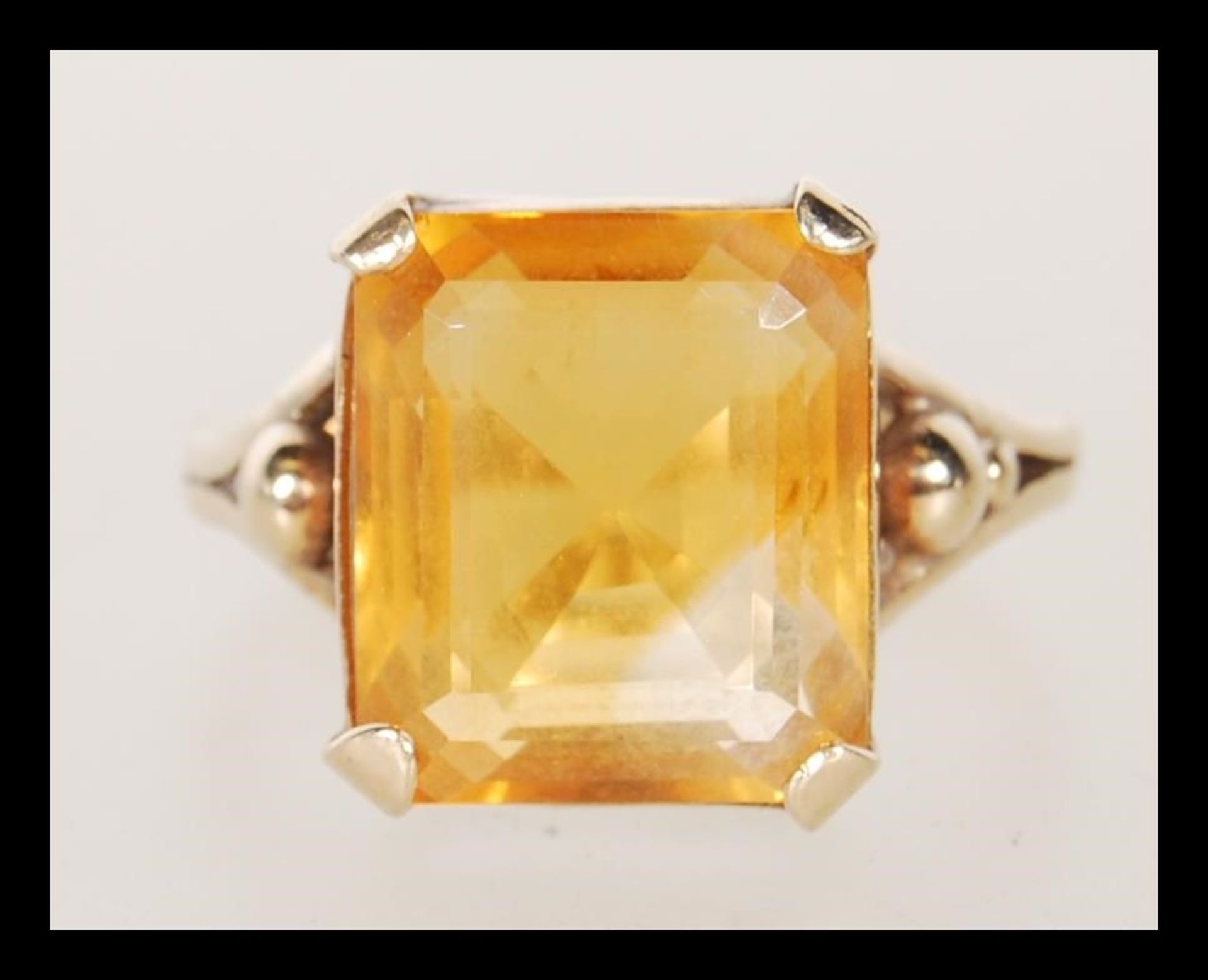 A 9ct gold dress ring, prong set with a square cut orange stone on a split shank mount. Unmarked but