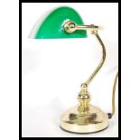 A vintage 20th century bankers desk lamp having an adjustable green glass shade raised on a brass