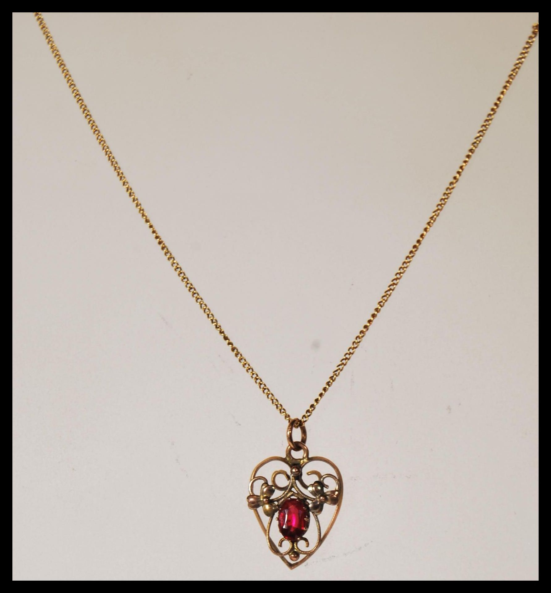 A 9ct gold openwork heart shaped pendant necklace, having a red stone to centre, with floral design,