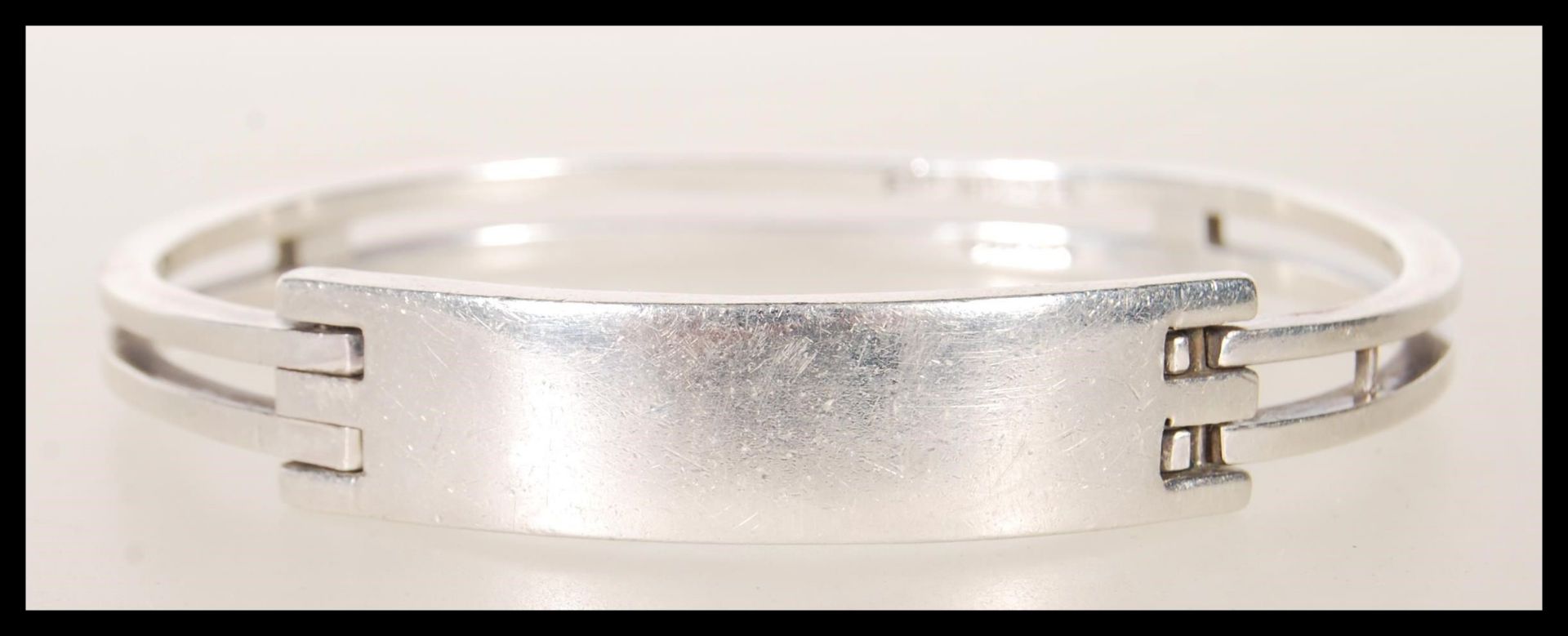 A stamped 925 silver bangle bracelet having square bars culminating in a square geometric clasp.