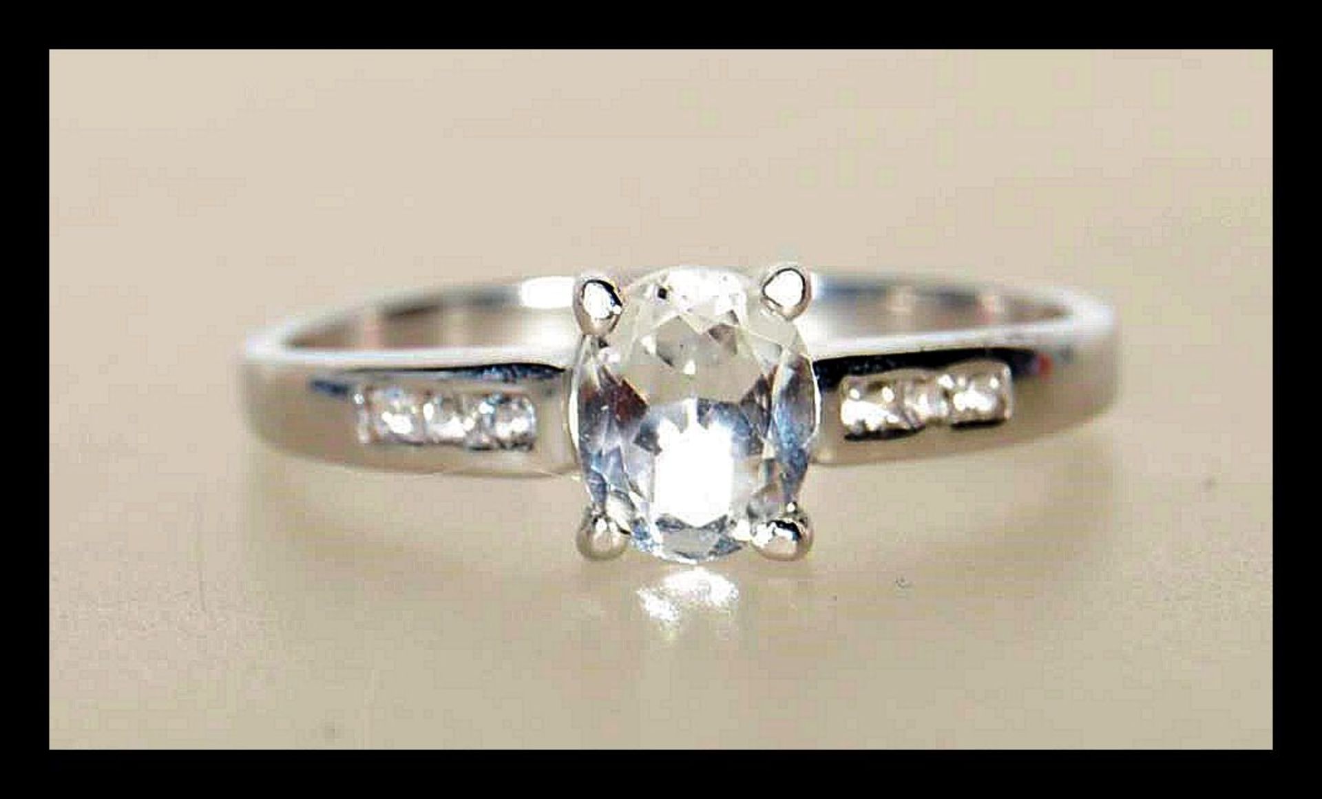 A hallmarked 9ct white gold ladies ring prong set with a oval cut white stone having accent stones