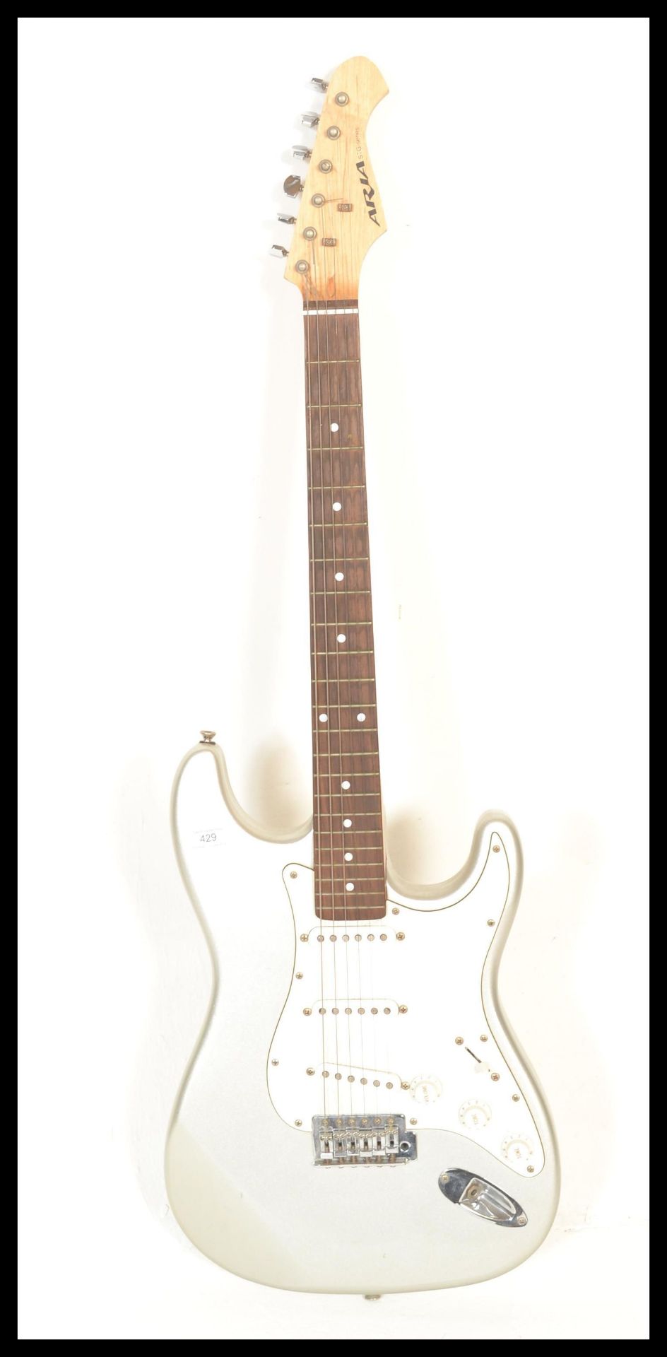 An Aria six-string STG Series electric guitar, silver body with white scratch guard and pick up.