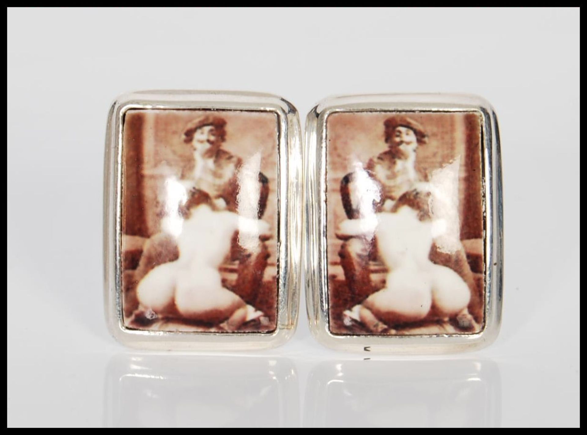 A pair of sterling silver and enamel cufflinks depicting an erotic scene involving a nude lady.