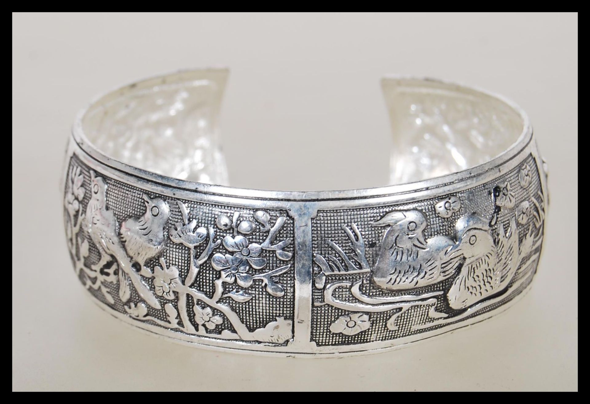 A Chinese silver bangle having panels of repousse decoration of animals including mandarin ducks,