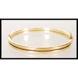 A stamped 9ct gold bangle bracelet having a hinge opening constructed from two bands with a catch to