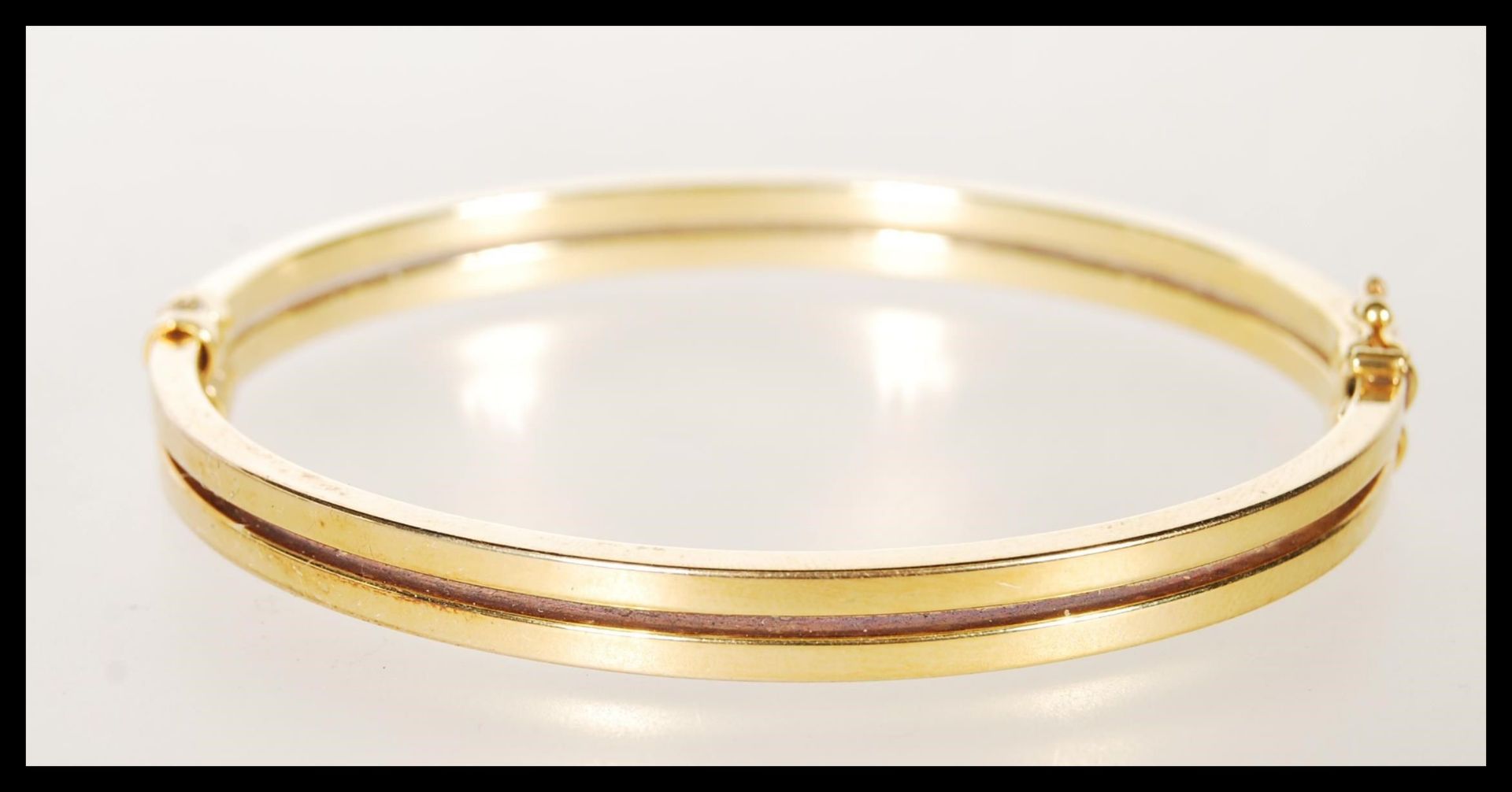 A stamped 9ct gold bangle bracelet having a hinge opening constructed from two bands with a catch to