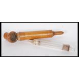 A early 20th Century treen / olive wood cased glass syringe, having screw top to the case.