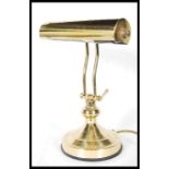 An Antique 20th Century style brass effect bankers lamp, having tubular shade and adjustable stem,