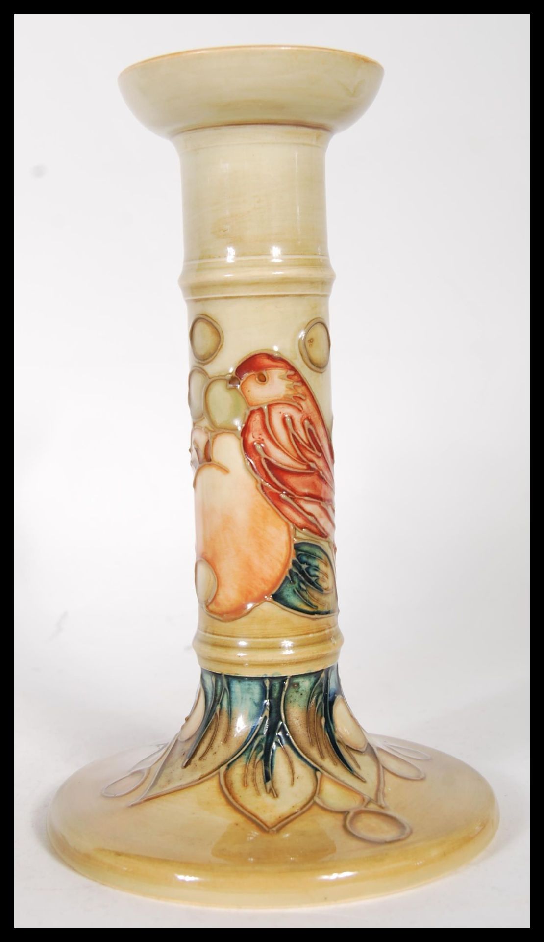 A Moorcroft pottery tube lined pedestal candlestick, decorated with a bird amongst fruit,