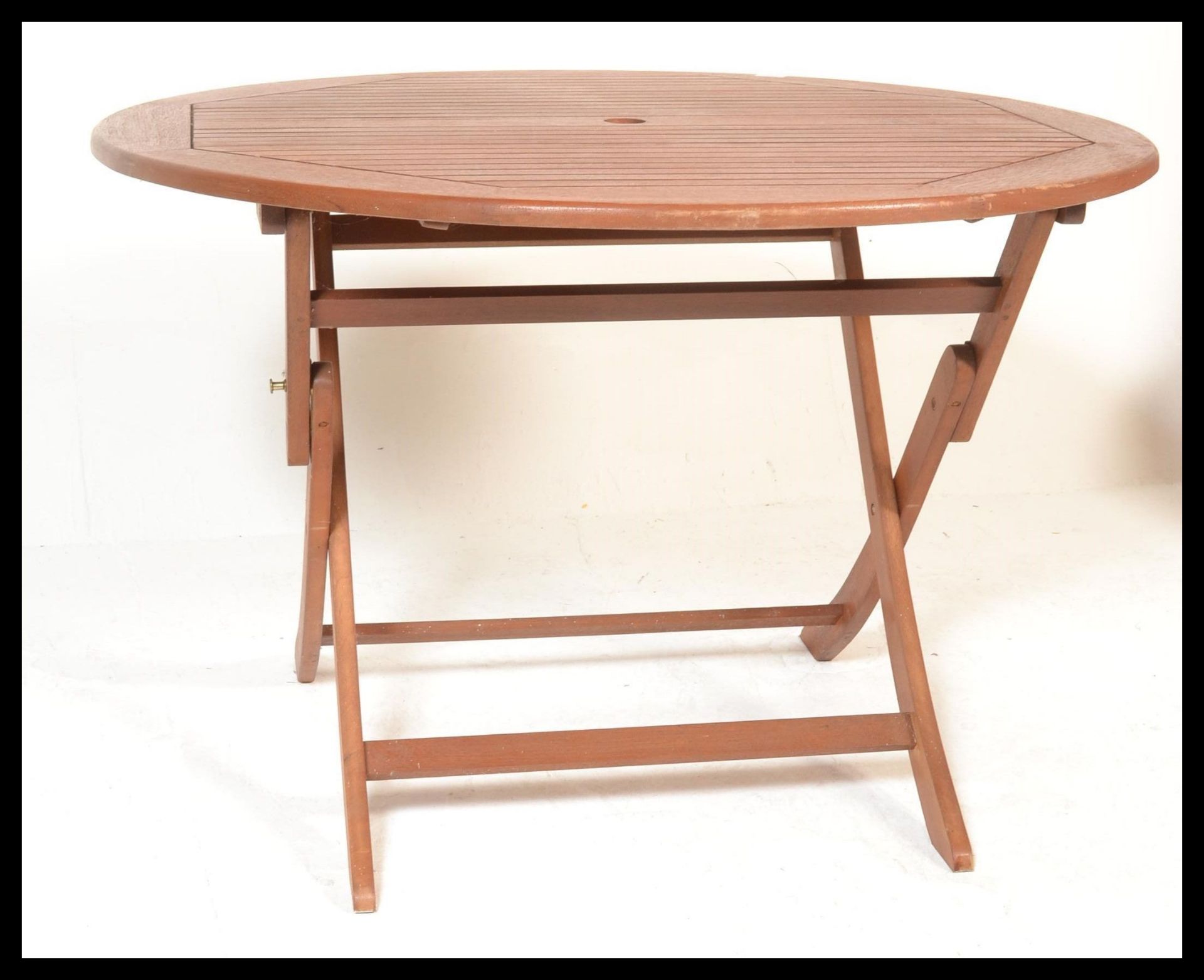 A contemporary teak wood outdoor garden table of circular form, raised on  a folding X-frame base