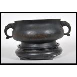 A Chinese bronze censer bowl of squat globular form with shaped twin handles, raised on a circular