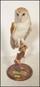 An early 20th Century taxidermy barn owl being raised on a turned wooden base, the owl perched on