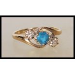 A stamped 9ct gold crossover ring set with a round cut blue topaz stone flanked by two illusion
