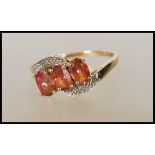 A stamped 375 9ct cross over gold ring set with three oval cut pink mystic topaz stones, having