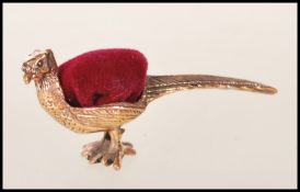 An unusual pin cushion in the form of a pheasant. The brass body with a red baize cushion top.