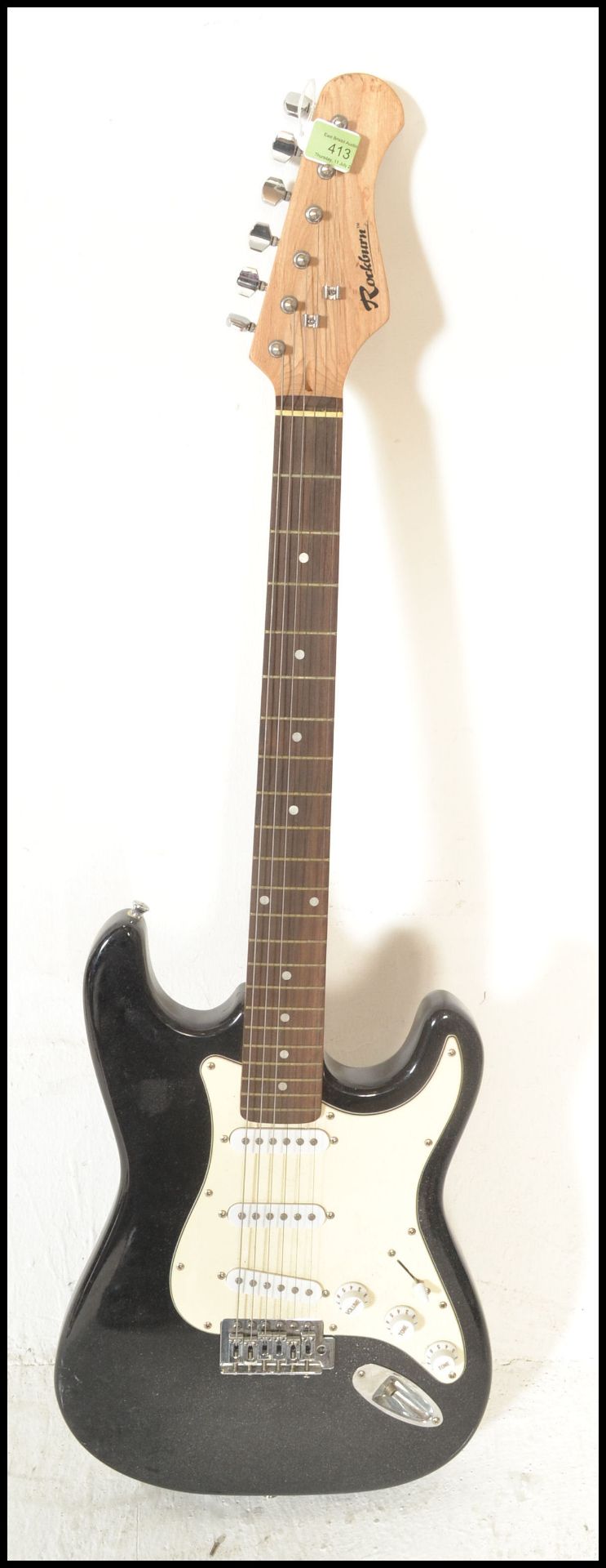 A vintage Rockburn electric six string guitar. The black body having white scratch guard with chrome