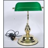 A vintage style bankers desk lamp having an adjustable green glass shade raised on a brass support