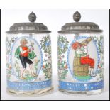 A pair of early 20th Century German glass and enamel over painted steins. Each with fitted pewter