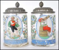 A pair of early 20th Century German glass and enamel over painted steins. Each with fitted pewter