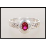 A ladies silver and cubic Zirconia ring. The silver rub over setting surrounding a coloured red