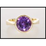 A hallmarked 18ct gold ladies dress ring bezel set with a round cut purple synthetic sapphire..
