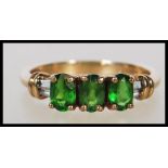 A hallmarked 9ct gold ring set with three oval cut green stones between white stone shoulders.