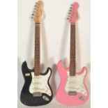 Two 20th Century Stratocaster style six string guitars by Encore, one having a pink body and the