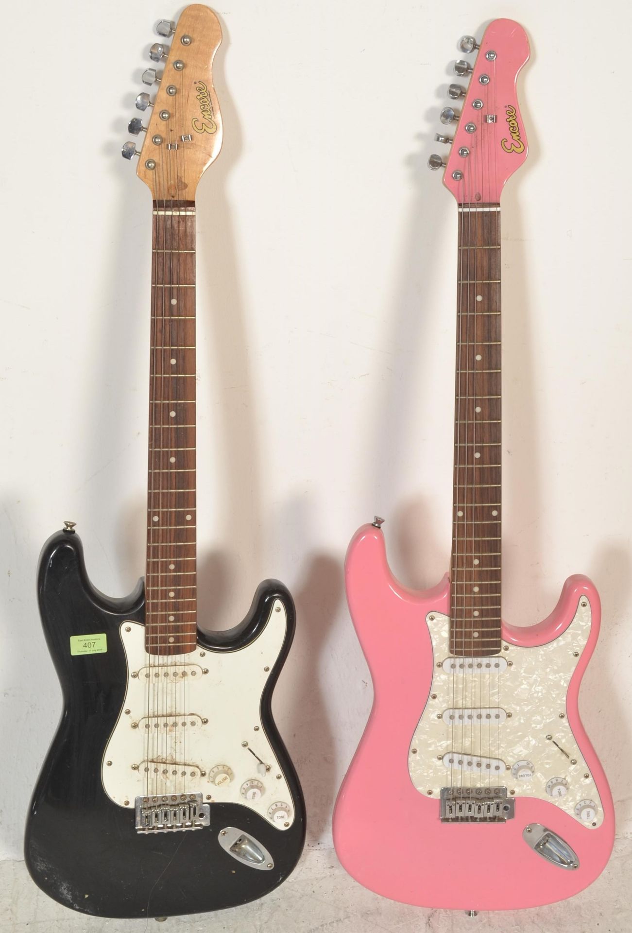 Two 20th Century Stratocaster style six string guitars by Encore, one having a pink body and the