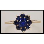 A hallmarked 9ct gold ring having a flower head of blue sapphires (synthetic). Hallmarked