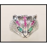 A silver ring in the form of a cats head with emerald eyes and channel set ruby's to the head.