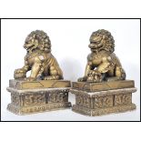 A pair of gilt temple dogs / foo dogs, both posed upon pedestal bases with their paws upon a