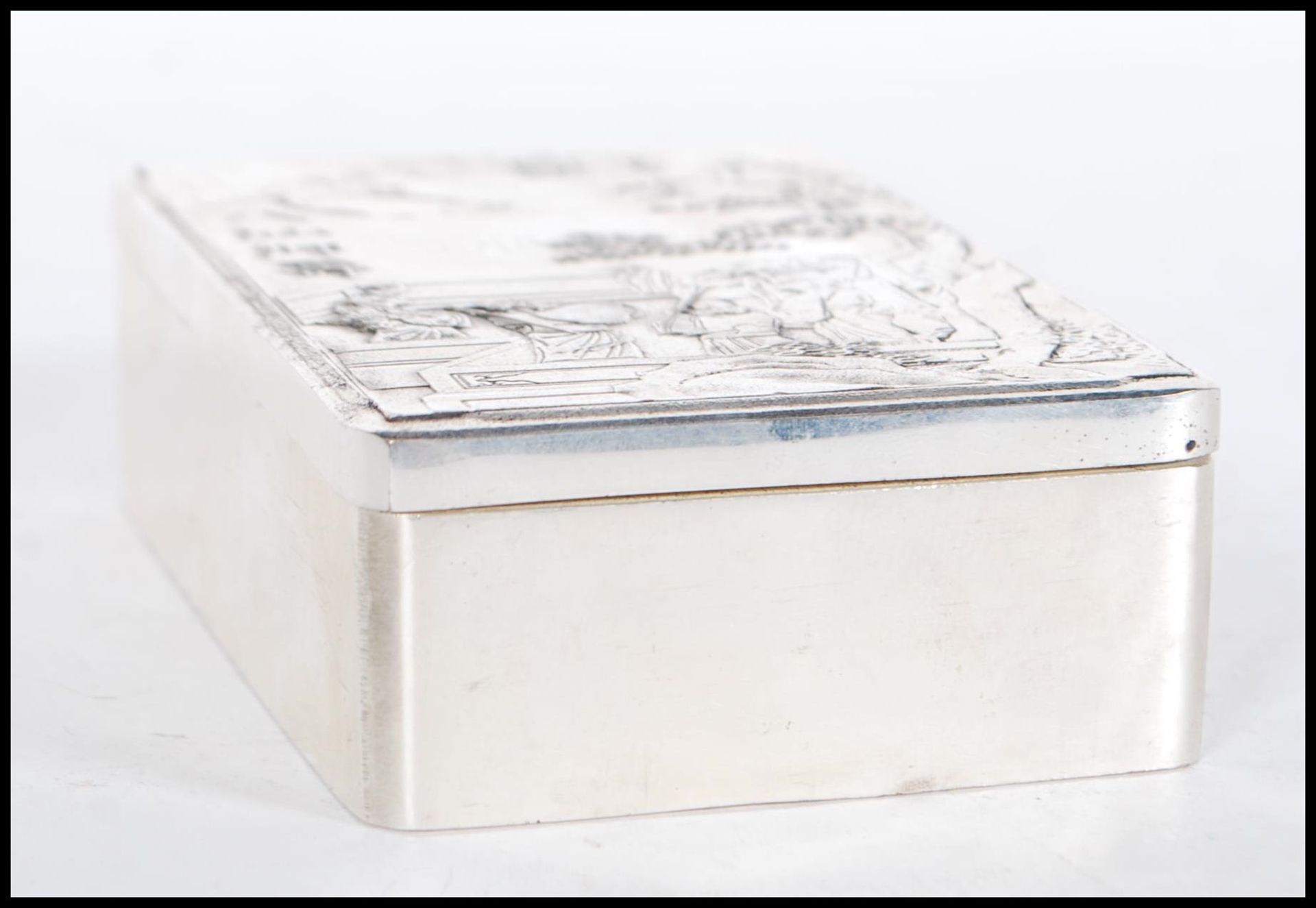 A silver white metal Chinese trinket box, the lid having relief oriental scene decoration