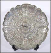 A vintage silvered brass wall charger plate having repousse decoration, central cartouche with
