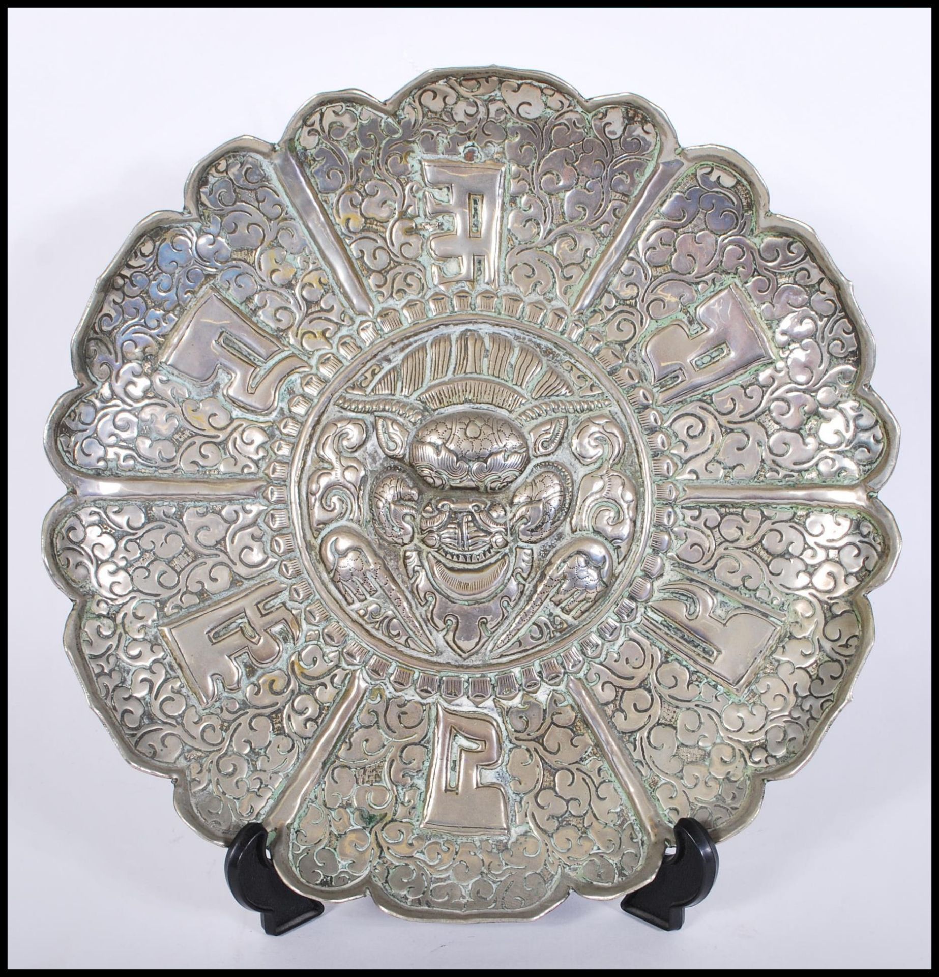 A vintage silvered brass wall charger plate having repousse decoration, central cartouche with