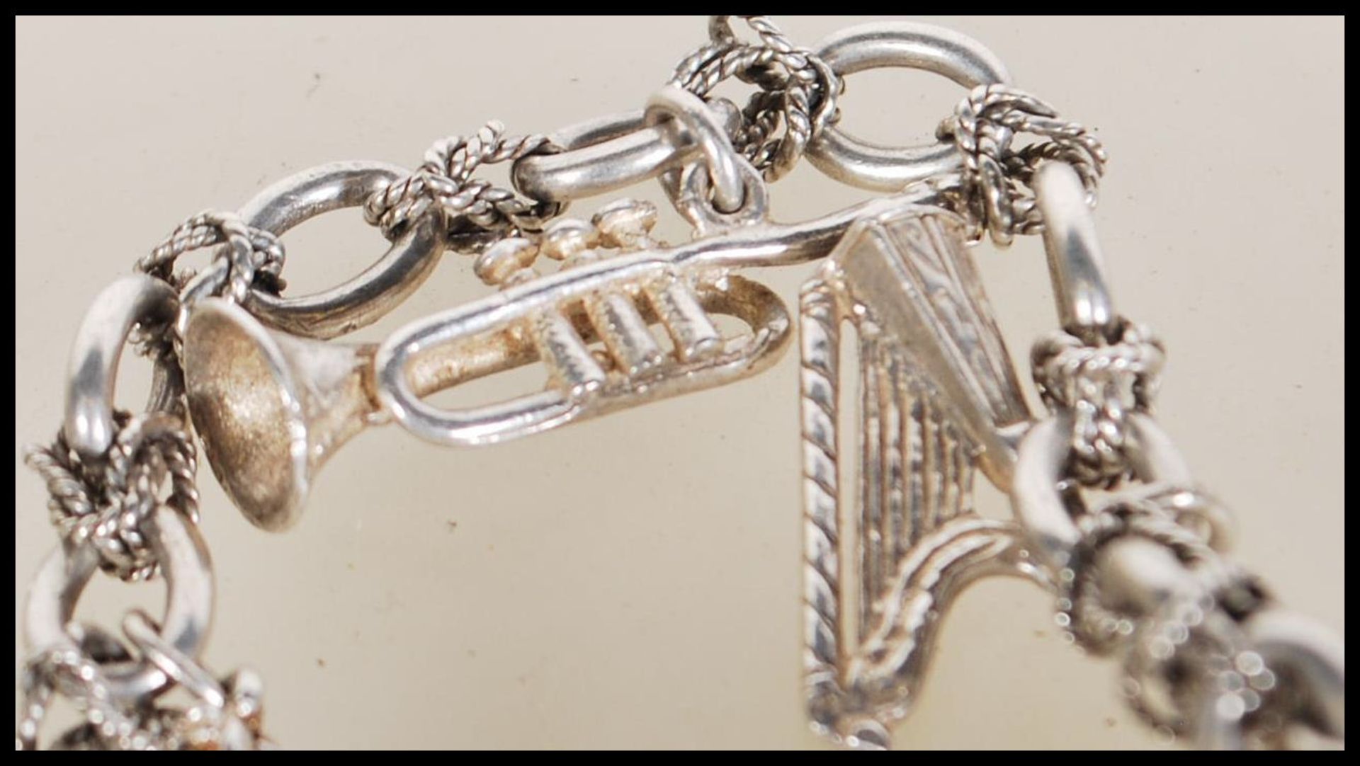 A silver charm bracelet having musical instrument charms to include trumpets, harp, bell violin, - Image 8 of 9