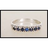 A hallmarked 9ct white gold ring set with a row of round cut blue stones. Hallmarked London 1976.