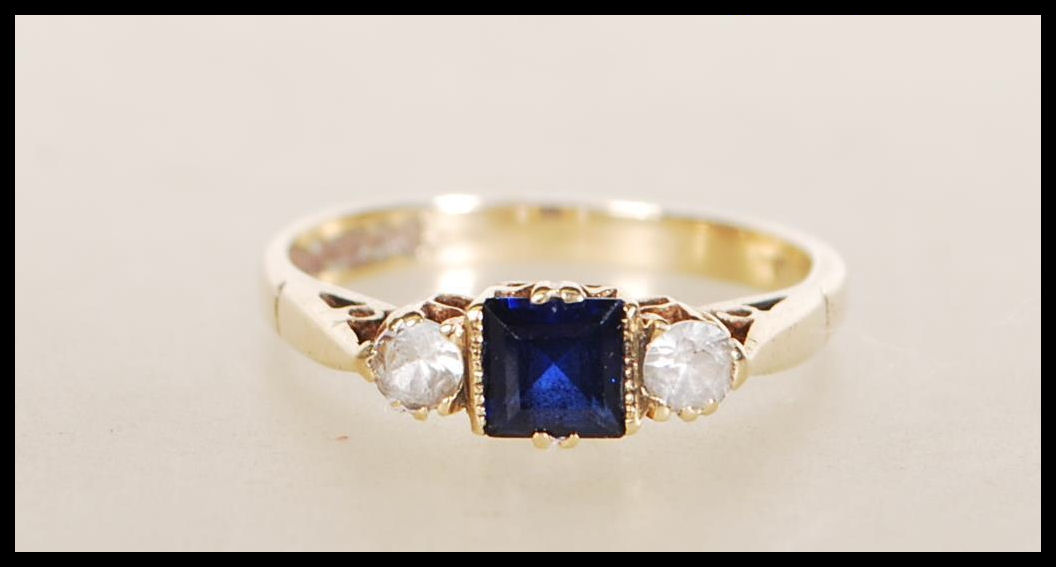 A hallmarked 9ct gold ring set with a square cut blue stone flanked by two round cut white stones.