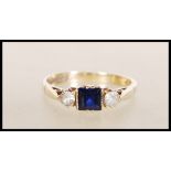 A hallmarked 9ct gold ring set with a square cut blue stone flanked by two round cut white stones.