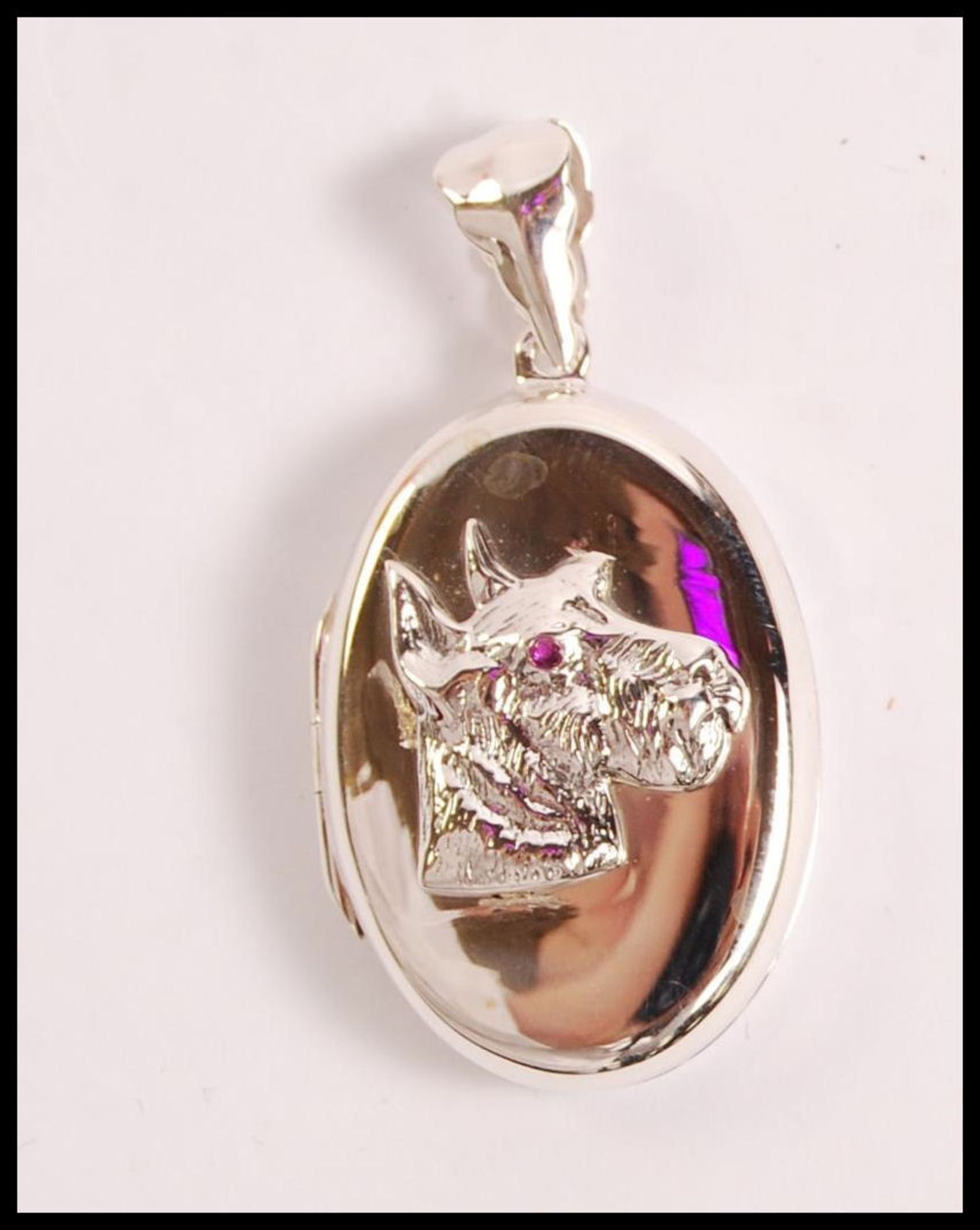 A stamped 925 silver locket of oval form having an embossed scottie dog set with a red stone eye.