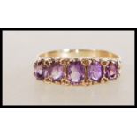 A hallmarked 9ct gold ring set with five oval cut amethyst in a scrolled decorative setting.