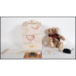 A boxed Steiff teddy bear titled 'The Million Hugs Bear' in copper brown wearing a burgundy scarf