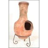 A 20th Century garden terracotta / clay tall Chiminea of bulbous form, set on a scroll work metal