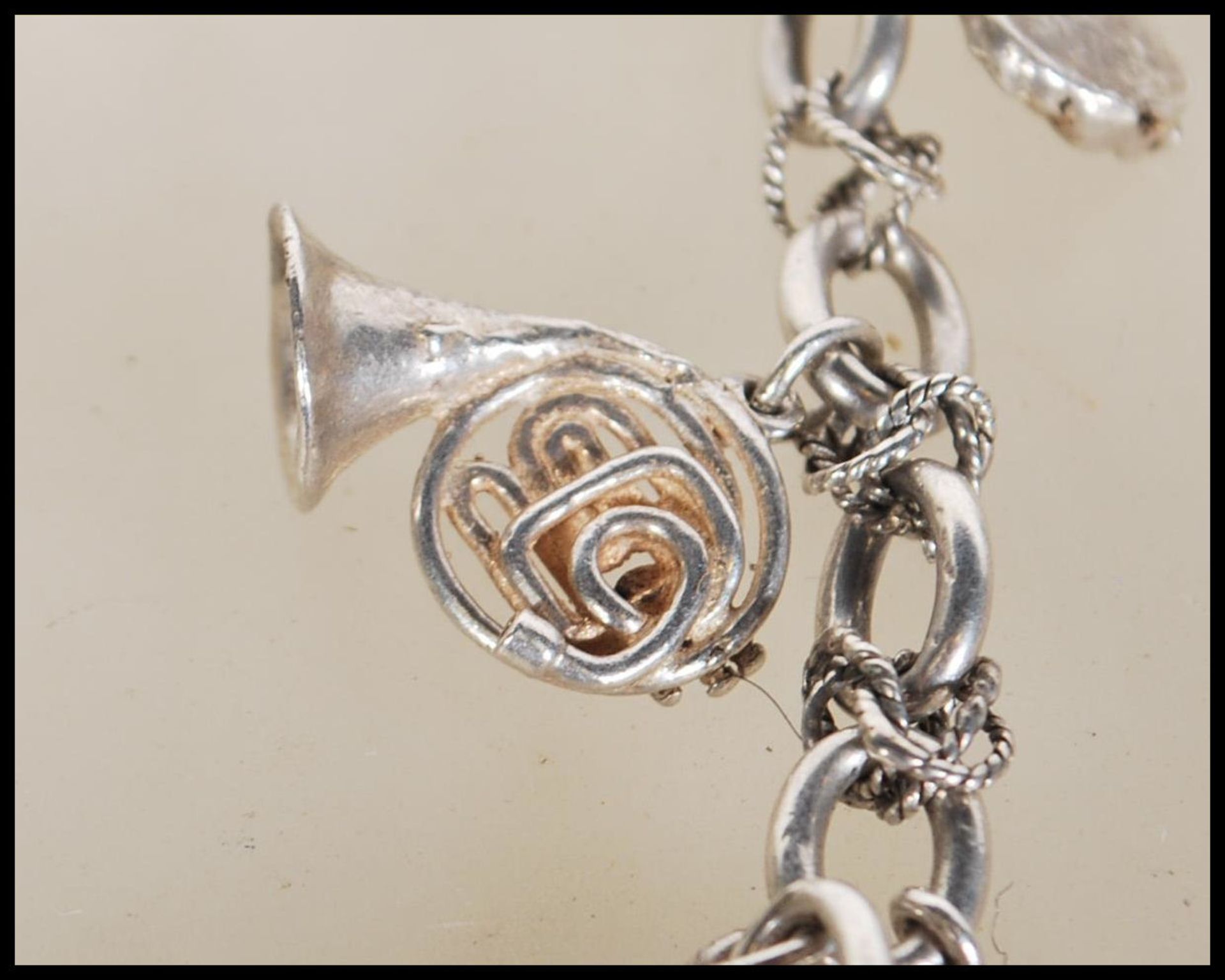 A silver charm bracelet having musical instrument charms to include trumpets, harp, bell violin, - Image 6 of 9