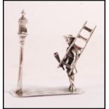 A sterling figurine depicting a lamplighter holder a ladder infront of a street light. Weight 15.9g.